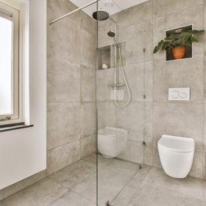 Marble bathroom with a small window a shower stall and toilet