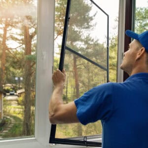 worker installing mosquito net wire screen on house window