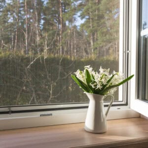 White window with mosuito net in a rustic wooden house overlooking the blossom garden.